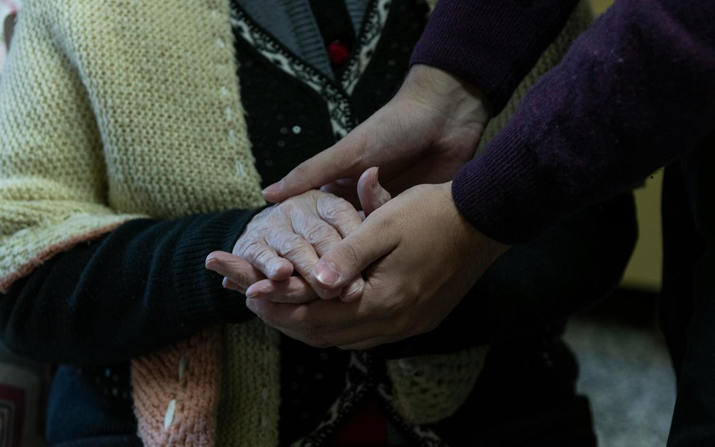 An adult holding the hands of an elderly adult.
